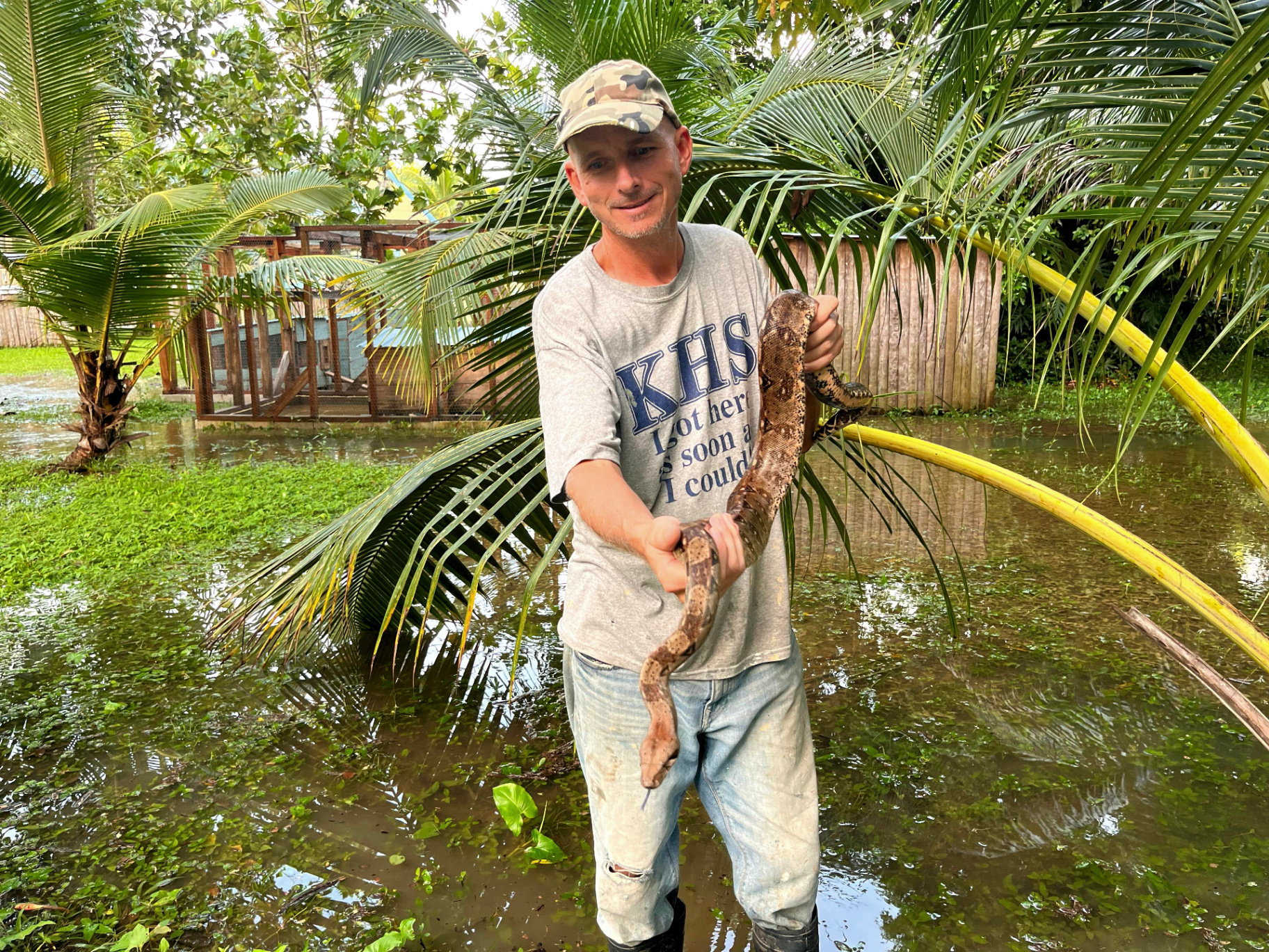 The author standing in a flooded Belize jungle holding a large snake.